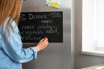 Young woman writing menu on chalkboard in kitchen