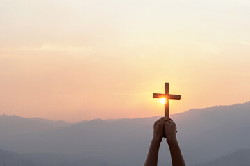 Silhouette human hand holding christian cross for worshipping God at sunset sky background....