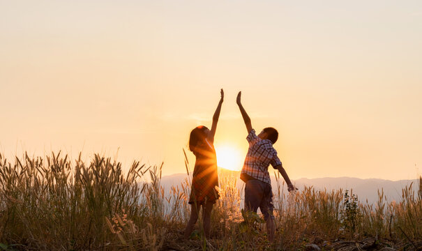 Silhouette of children playing with raised hands on the mountain at the sunset time.