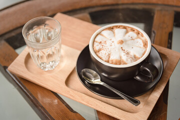 Porcelain cup of hot milk tea on wooden table as served with drinking water