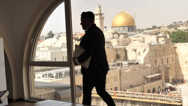 Jew with tallit bag walks across loft window with view on Jerusalem Temple Mount
