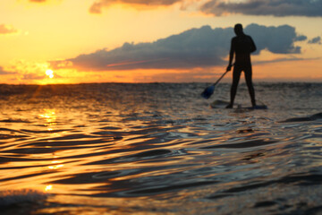 Stand Up Paddle Boarding In Japan at Sunrise and Sunset a solo rider keeping fit & healthy on the Pacific Ocean in a black wetsuit, also catching some large waves, The ocean is blue with a nice sky.