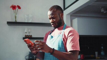 Disappointed young african man using a smartphone, receiving a negative message can't believe stands in the kitchen. Bad Internet news. Shock content. - Powered by Adobe