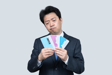 A middle-aged Asian businessman holding a bank passbook in his hand on a gray background.