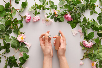 Female hands with perfume and flowers on light background