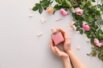 Female hands with perfume and flowers on light background