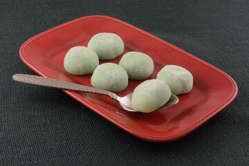 Green tea ice cream mochi balls on red serving dish with serving spoon