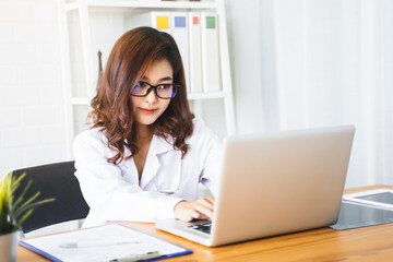 Medical health clinic beautiful Asian doctor working using laptop typing, stethoscope diagnosing patient analysis writing on form contract healthcare provider service insurance busy in modern office