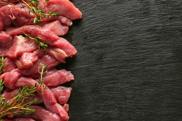 Pieces of fresh beef meat with herbs on dark background
