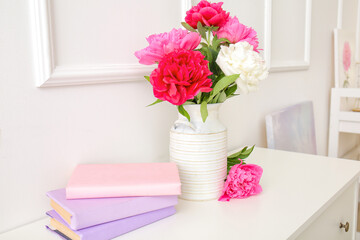 Vase with beautiful peony flowers and books on table in room