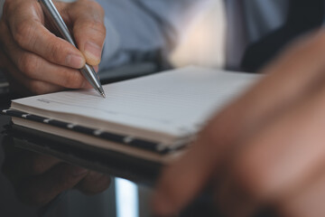 Close up of businessman hand with a pen writing his work plan on notebook in office