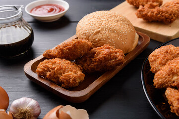 Fried breaded chicken wings with hamburger bread on wooden table.