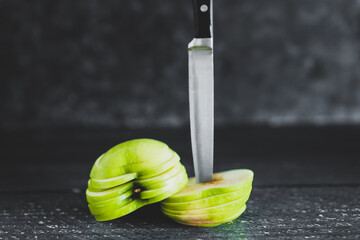 food ingredients concept, green apple cut into thin equal slices stacked into two halves with knife
