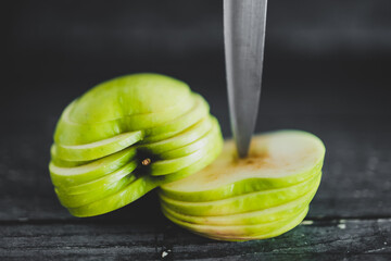 food ingredients concept, green apple cut into thin equal slices stacked into two halves with knife