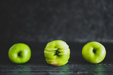 food ingredients concept, green apples lined up on wooden table with centered one cut into slices