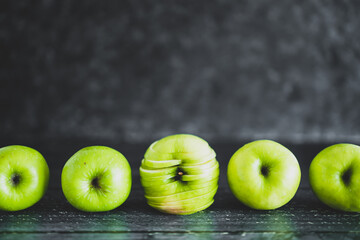 food ingredients concept, green apples lined up on wooden table with centered one cut into slices