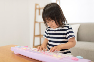 おもちゃのキーボードを弾いて遊ぶ3歳の女の子