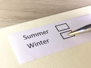 One person is answering question on a piece of paper. The person is thinking to prefer summer or winter.