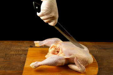 Woman cuts chicken carcass with a knife on a wooden board. © finist_4