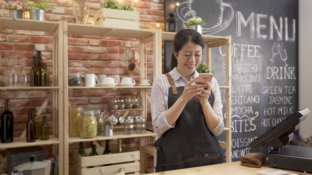 Technologies make life easier. beautiful woman waitress in apron using smart phone with smile while standing at counter in cafe store. barista laughing while chatting on cellphone in coffee shop