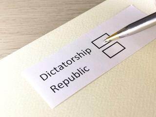 One person is answering question on a piece of paper. The person is thinking to choose  dictotorship or republic.