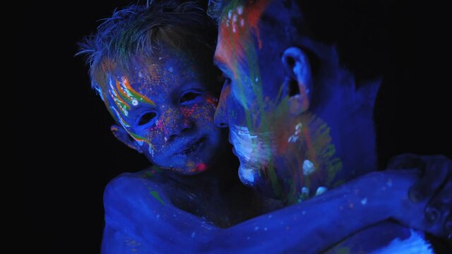 Portrait of a child and a man with fluorescent bright drawings on the body in the dark with neon light. Young father and son are painted with UV paint.