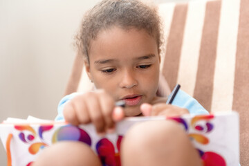 Little girl drawing at home sitting on chair.