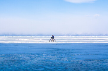 A man doing solo outdoor activity, enjoying time alone in nature, riding a bicycle on frozen lake in winter, wide angle image