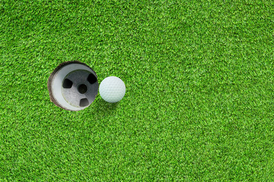 Top View White Golf Ball On Green Grass Meadow Field Nearly Hole.