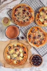 Pizza with olives on paper and wire rack on a gray background with a bottle of oil and sauce top view