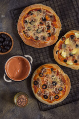 Pizza with olives on paper and wire rack on a dark background with a bottle of oil and sauce top view