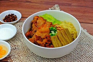 Egg noodles with braised chicken wings and bitter gourd noodle soup ready to be served with condiments on wooden table.