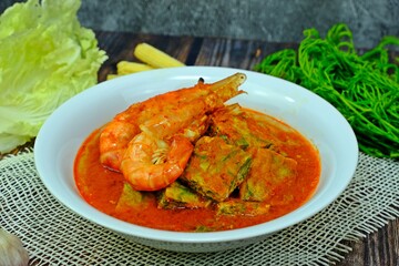Authentic Thai sour curry with shrimps and acacia omelet having various vegetables displayed aside.