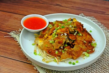 Crispy fried mussels pancake served with chilli sauce on wooden table.