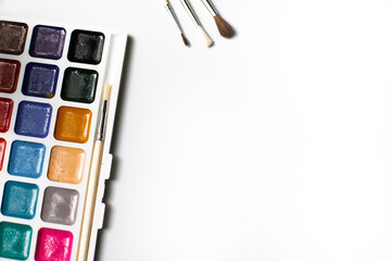 A palette of eighteen-color watercolors and paintbrushes on a white background with space for text.
