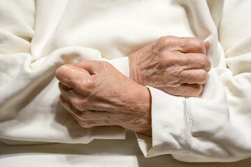 Hands of an elderly woman clenched in fists on her chest.