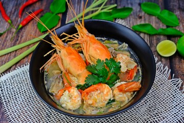 Authentic Tom Yum Kung, popular and delicious Thai hot spicy soup with shrimp, mushrooms and Thai herbs condiments on wooden table.