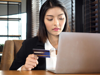 Fototapeta premium Asian business woman in suit using credit card shopping online with computer laptop in coffee shop cafe.Young female shopping online and paying with a credit card. 