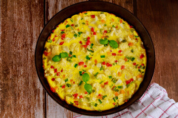 Homemade omelette with vegetables in pan on wooden background.