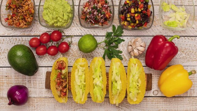 Making delicious hard shell tacos - with the filling ingredients in bowls, stuffing and assembling the popular mexican dish - top view, stop motion animation