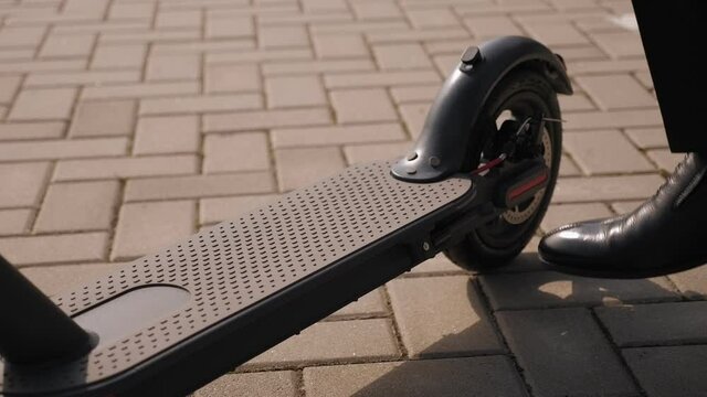Close-up of a businessman in black leather shoes walks up to the electric scooter and removes the stand with his foot. Businessman rides an electric scooter. Slow motion.