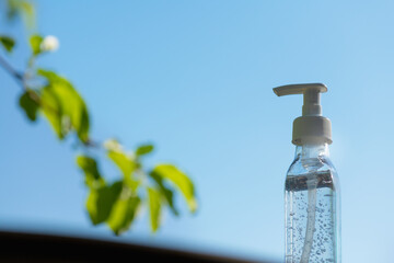 Antibacterial gel in a white transparent package with a spray against the blue sky with a tree branch. Concept of cleanliness and fight against coronavirus infection