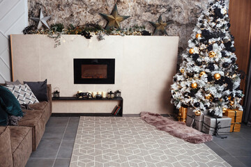 The gray velor sofa in the dark loft room has a bright light from the eternal light and an artificial fireplace. Inner attic with concrete walls and a decorated Christmas tree with gift boxes.