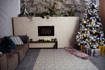 The gray velor sofa in the dark loft room has a bright light from the eternal light and an artificial fireplace. Inner attic with concrete walls and a decorated Christmas tree with gift boxes.