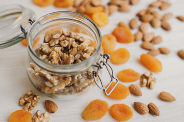 Glass jar with raw walnut and dried apricot and almond on wooden table. Food storage. Plant based snack