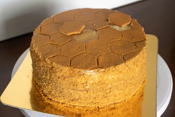 Whole honey medovik cake with hexagon honeycomb design. Cake on a golden plate on a wooden table.