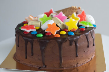 Colourful cake with vibrant decorations on top. Chocolate cake decorated with colourful candies topping. Vibrant kids birthday cake golden plate.