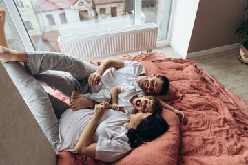 Pregnant mother playing with her child in the bedroom.Family are sharing good emotions while relaxing at home Big window, natural light, terracotta bed linen. Have fun, kiss and hugs.