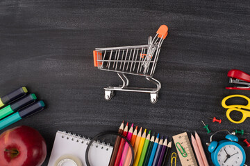 Back to school stationery shopping advert concept. Top above overhead view photo of small cart in center apple and colorful stationery isolated on blackboard with copyspace © ActionGP