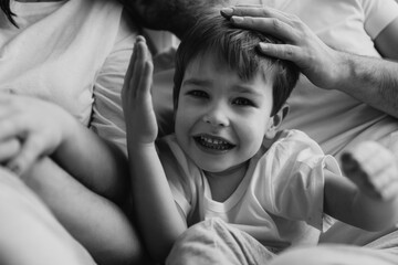 Close up portrait of a little smiling blond boy. He is playing with parents. Mother, father are sharing good emotions while relaxing at home Natural light. Black and white photo. Happy family.